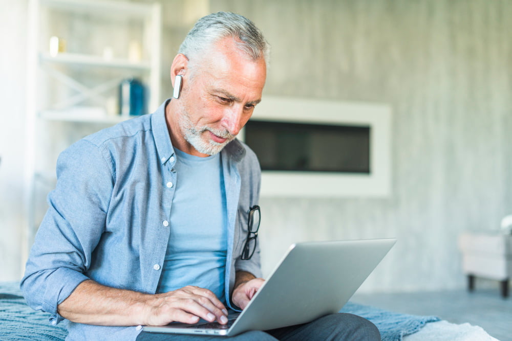 senior man with wireless bluetooth sitting bed using laptop