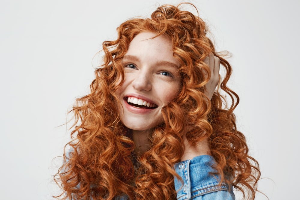 portrait cute happy girl smiling touching her curly red hair